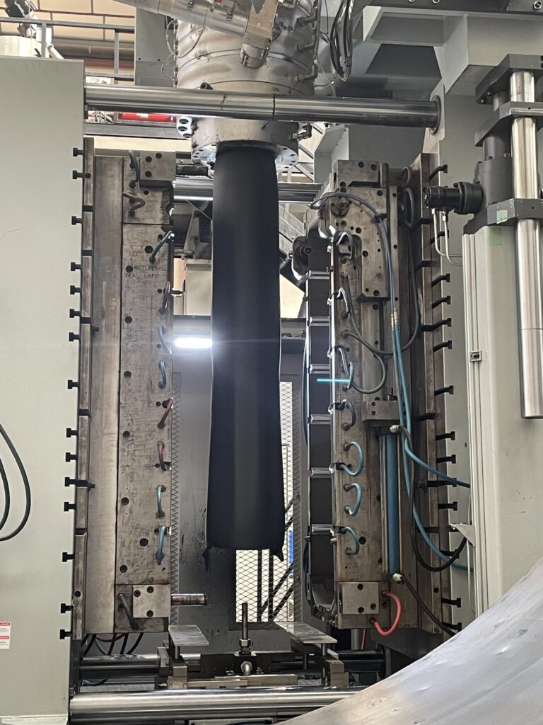 Paraison extrudée suspendue entre les deux demi-moules d'une souffleuse.