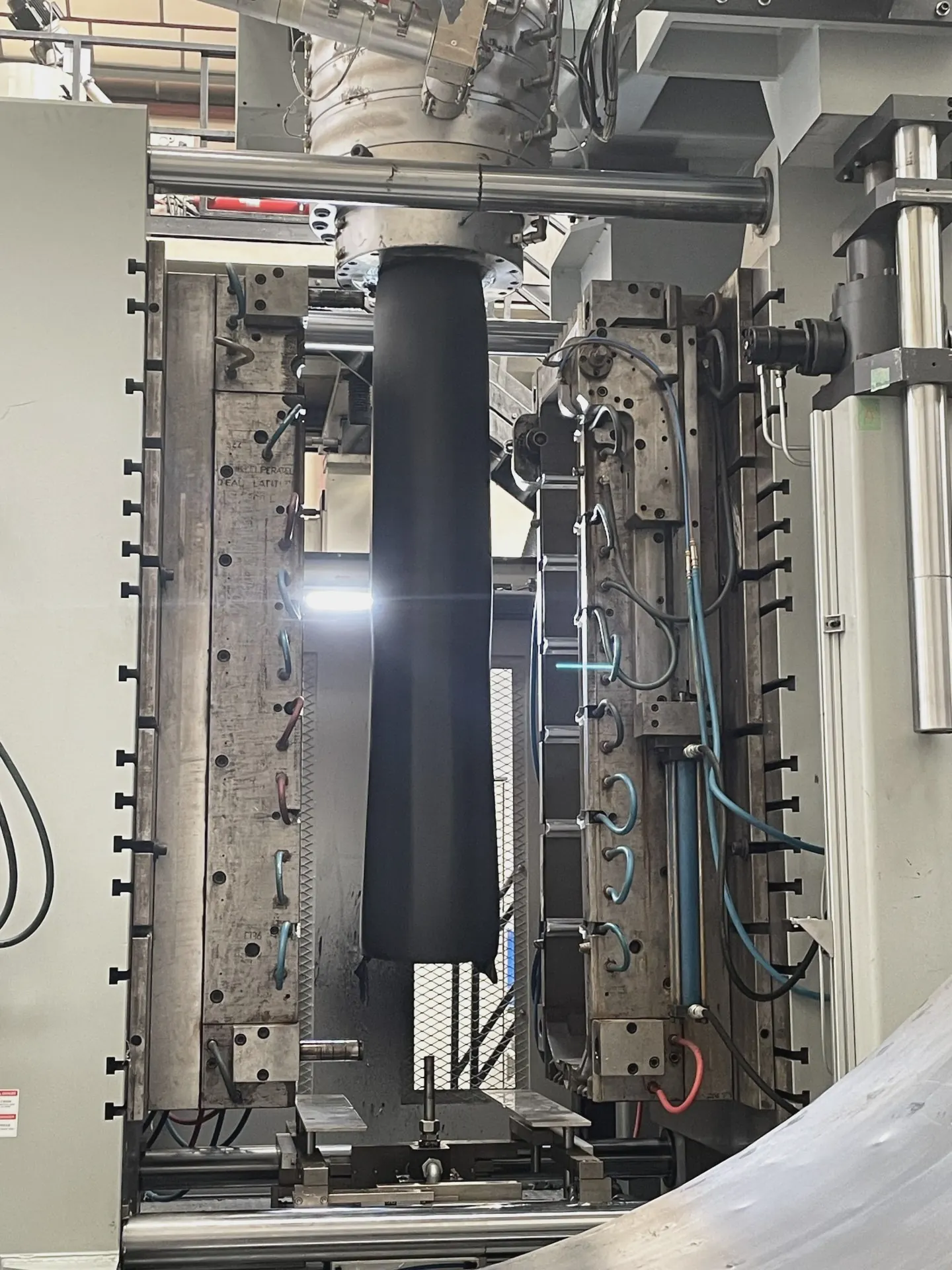 Paraison en cours d'extrusion dans un moule de soufflage ouvert, Plazur Industries.