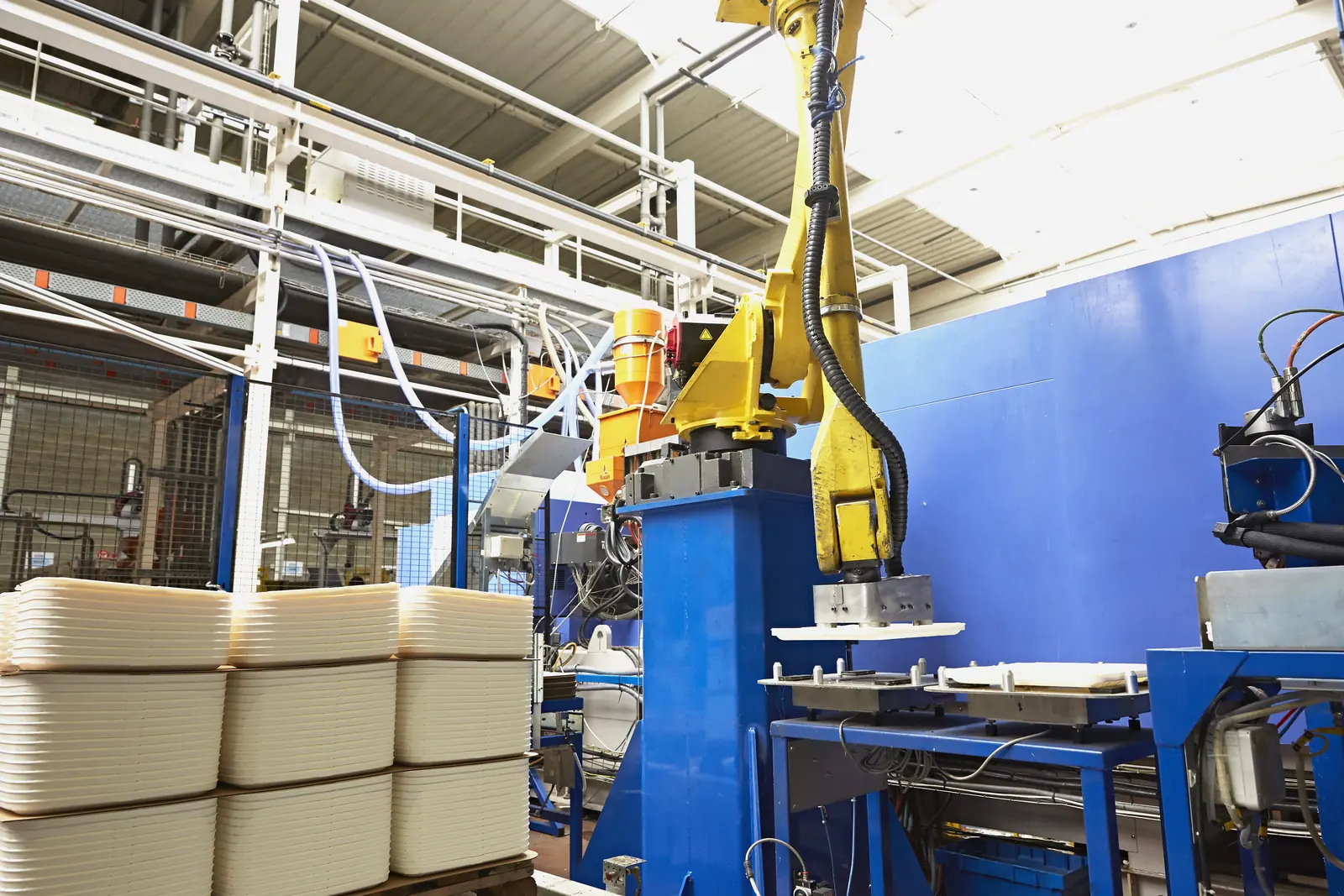Presse à injecter et robot de manipulation en sortie de production, avec pièces injectées empilées, atelier Plazur Industries.